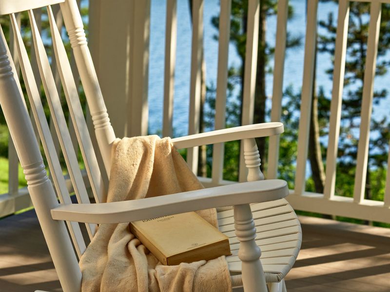 A white porch rocker with a book and a blanket, the lake beyond