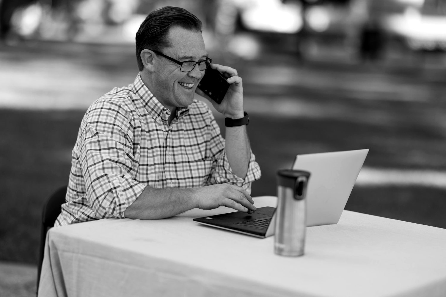 Dave Manley on a phone call at his laptop, smiling, outdoors