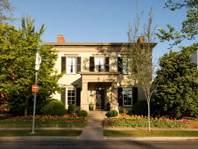 A colonial house with a porch on a sunny tree-lined street